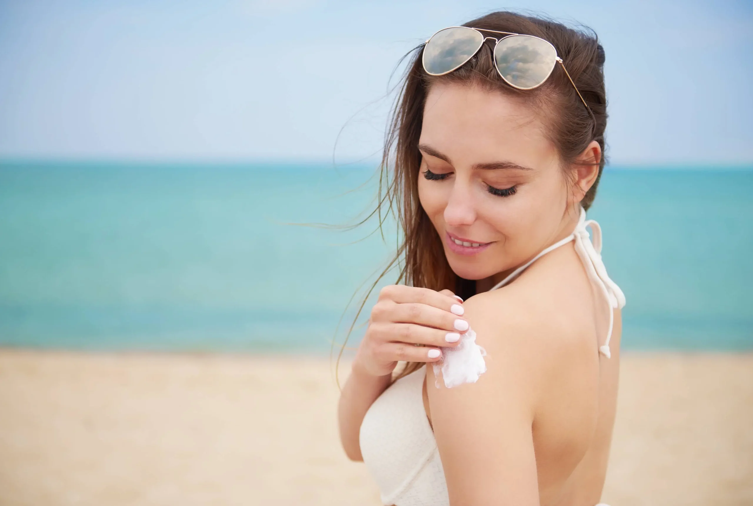 Woman applying sunscreen on shoulder at the beach for daily sun protection - Zicail Beauty Woman applying sunscreen on shoulder at the beach for daily sun protection - Gel vs Cream Sunscreen: Which One Is Better for You?
