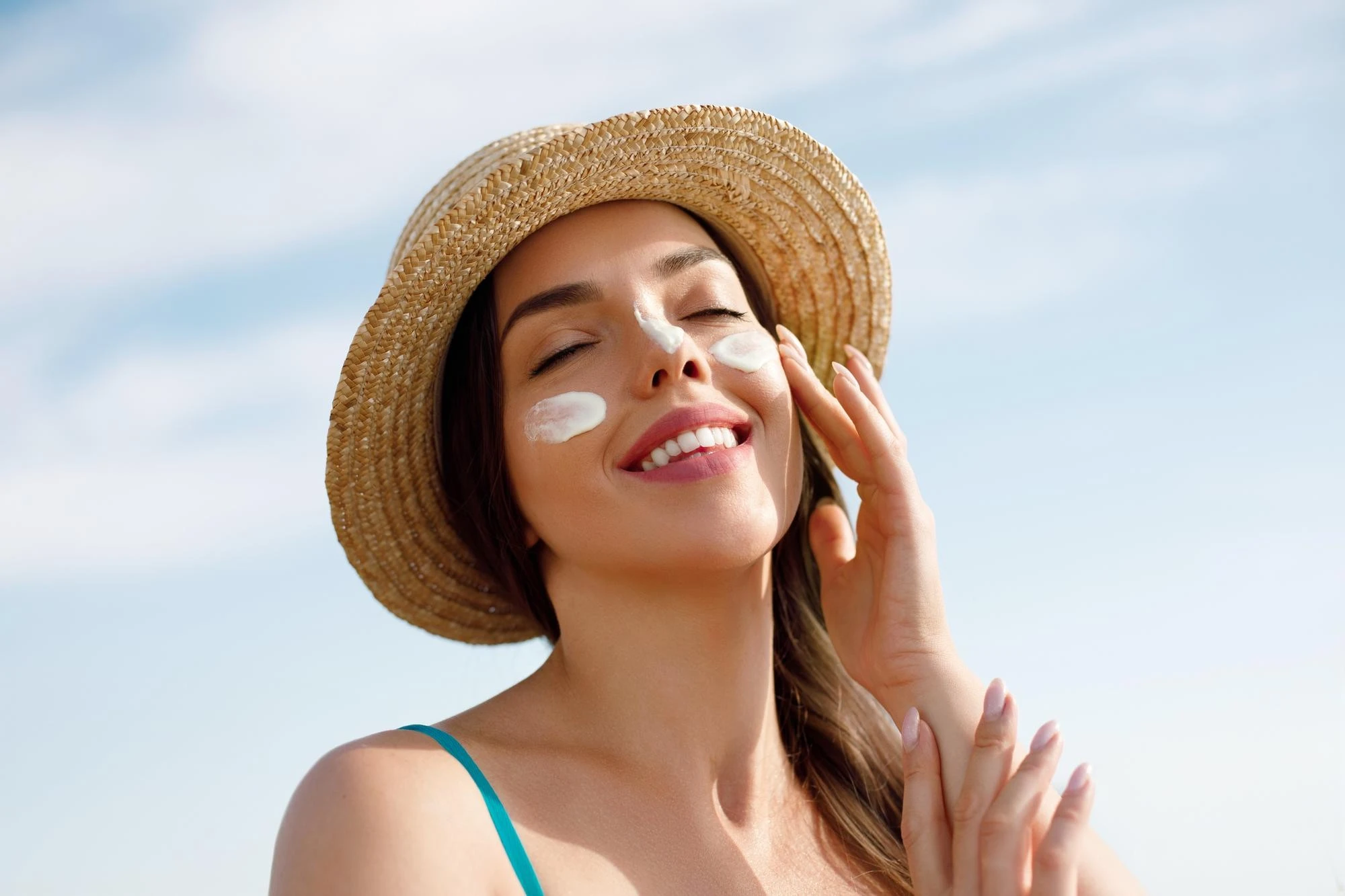 Woman applying sunscreen to her face while wearing a straw hat outdoors - Zicail Beauty Woman applying sunscreen to her face while wearing a straw hat outdoors - How Often to Reapply Sunscreen for Real Protection