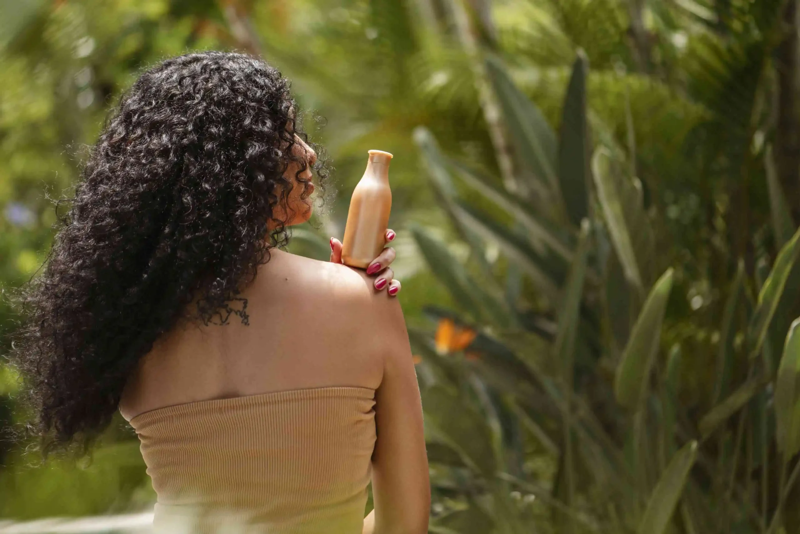 Woman holding sunscreen bottle outdoors for body sun protection in tropical setting - Zicail Beauty Woman holding sunscreen bottle outdoors for body sun protection in tropical setting - SPF 30 vs SPF 50: Which Sunscreen Should You Choose?